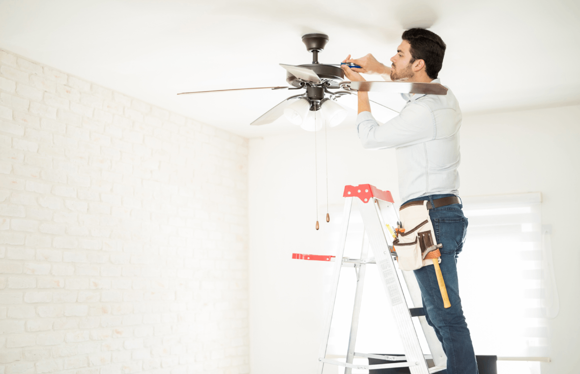 Man fixing ceiling fan on ladder.