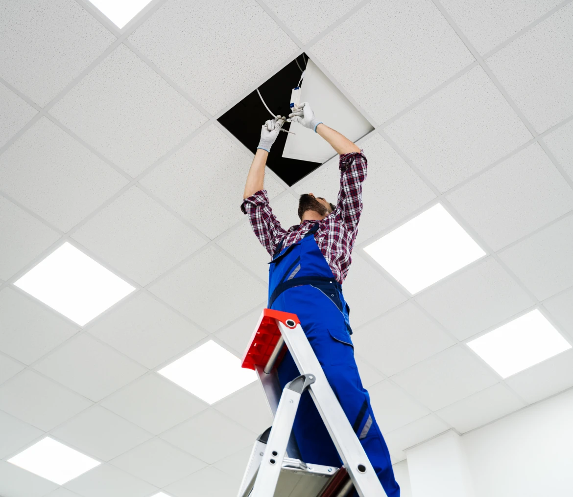 Worker installing cables in ceiling tiles