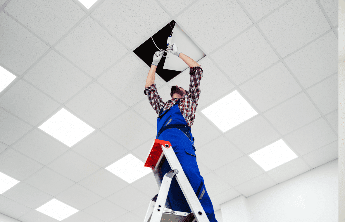 Worker on ladder fixing ceiling panel.