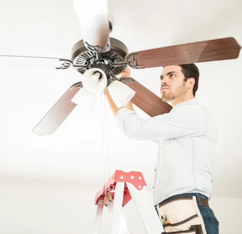 Man fixing ceiling fan on ladder.